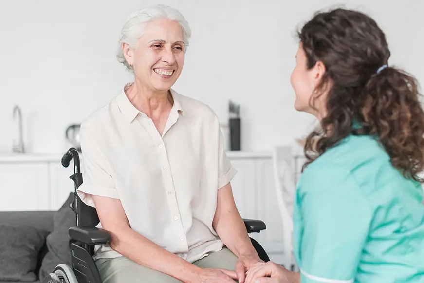 Healthcare professional holding hands with an older woman in a wheelchair